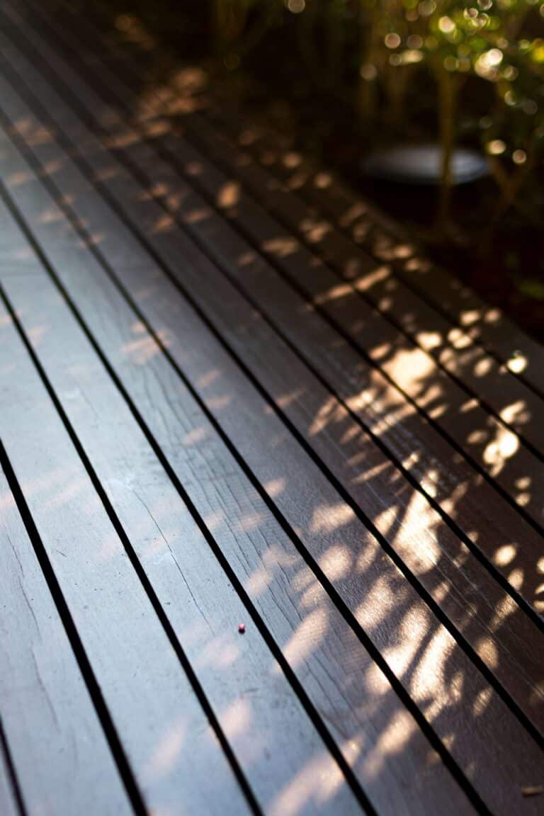 Close-up of weathered timber deck boards beside planters, showing grain, wear and colour variation.